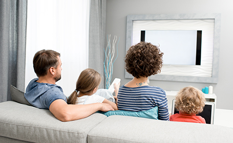 Back view portrait of family with two kids watching TV sitting on sofa in living room at home